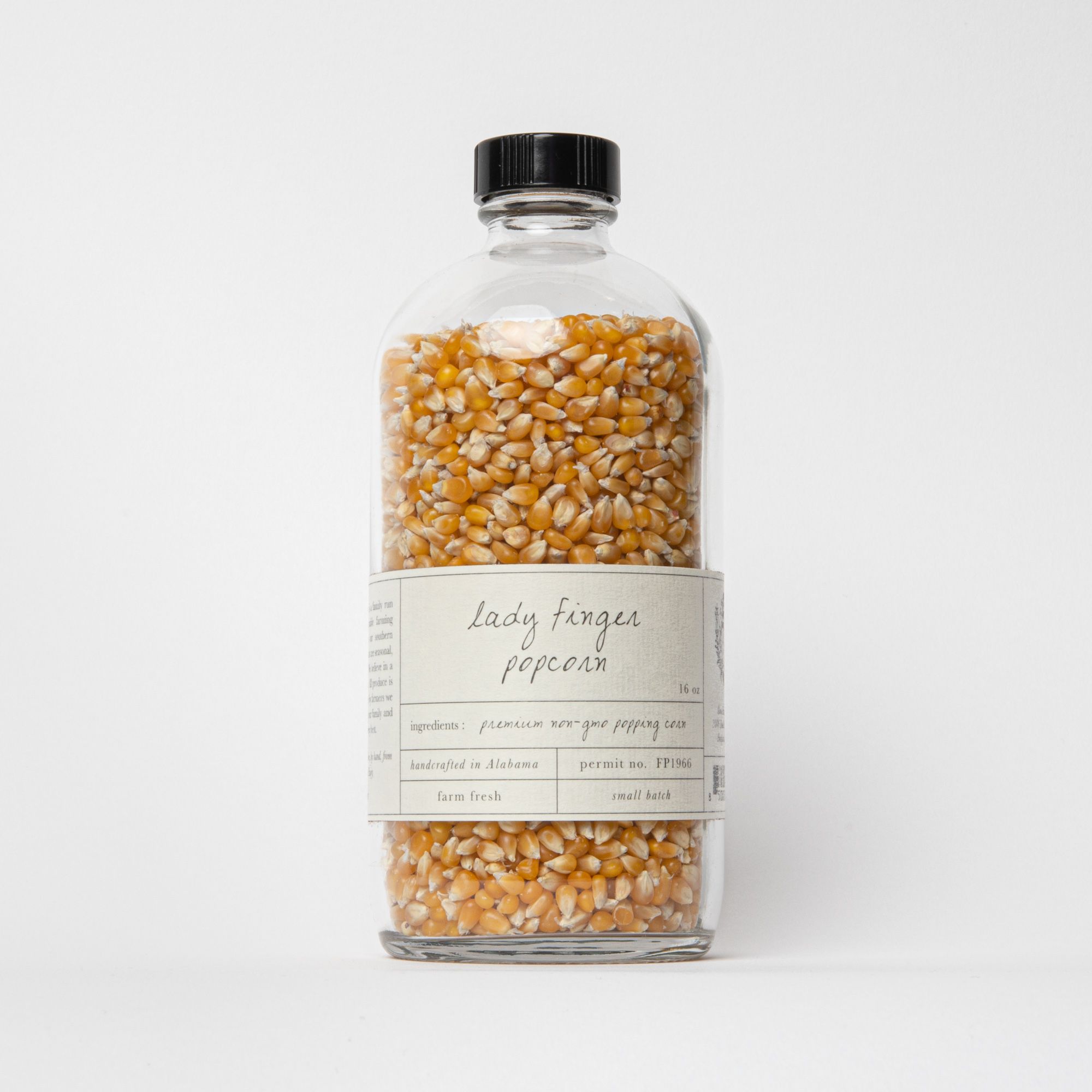 Glass bottle of popcorn kernels with an off white label that reads "Lady finger popcorn".