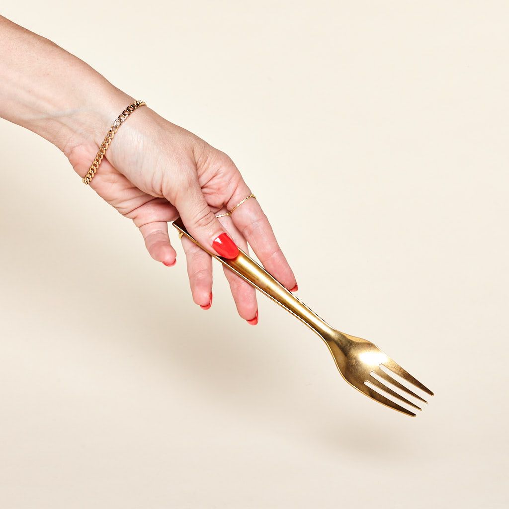 A hand holds a shiny brass fork