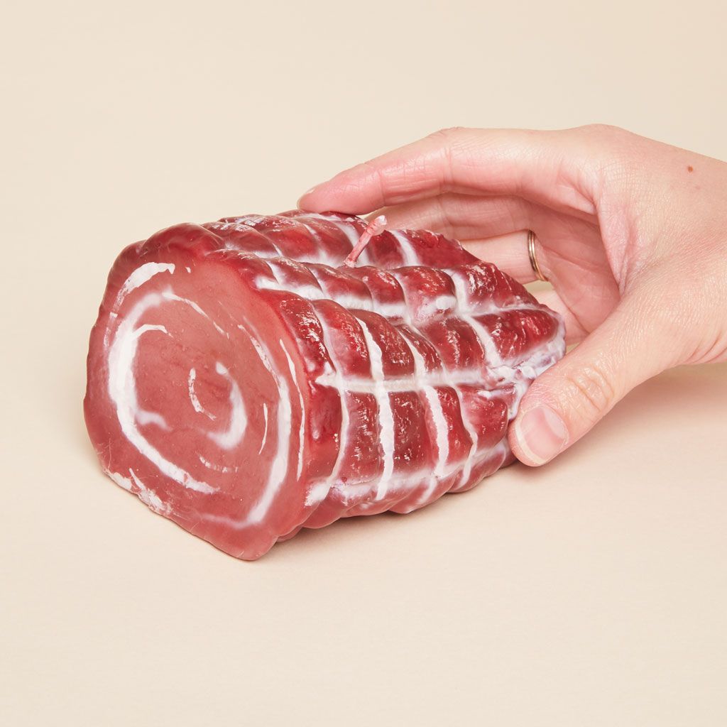 A hand holds a candle with the shape and coloring of an Italian meat called capicola