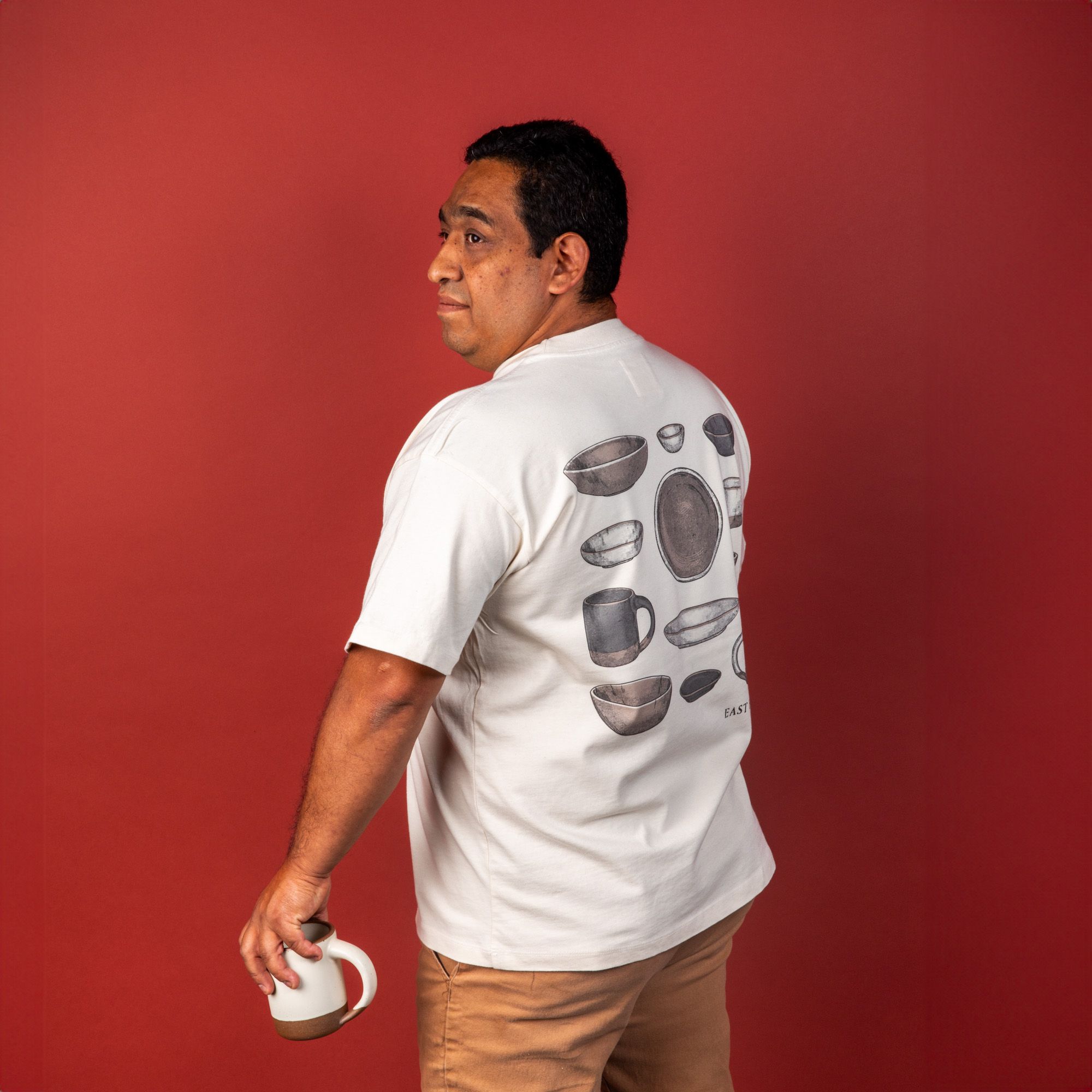 Model wearing the t-shirt shown from the back and holding a mug and looking off to the side