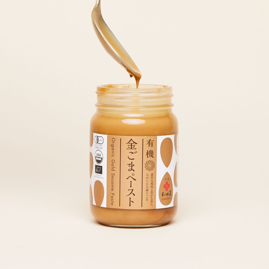 A spoon covered in sesame paste is poised above an open jar of the same sesame paste