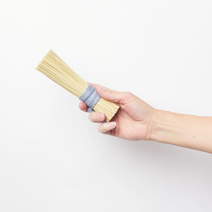Hand holding a pot scrubber made from a bundle of broomcorn tied at the handle with blue string
