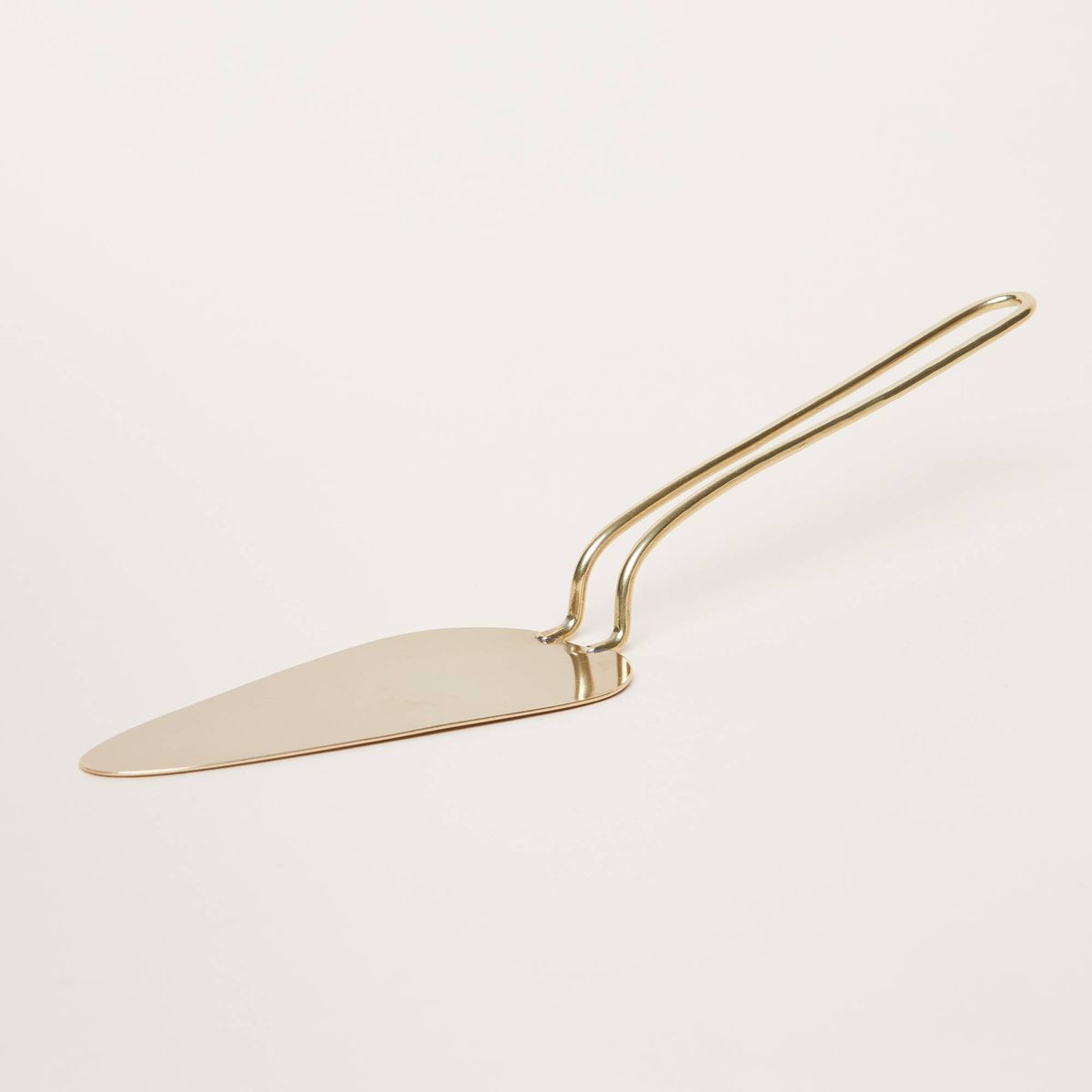 Crafted in brass, a triangular pie server has a long, thin loop of brass for a handle