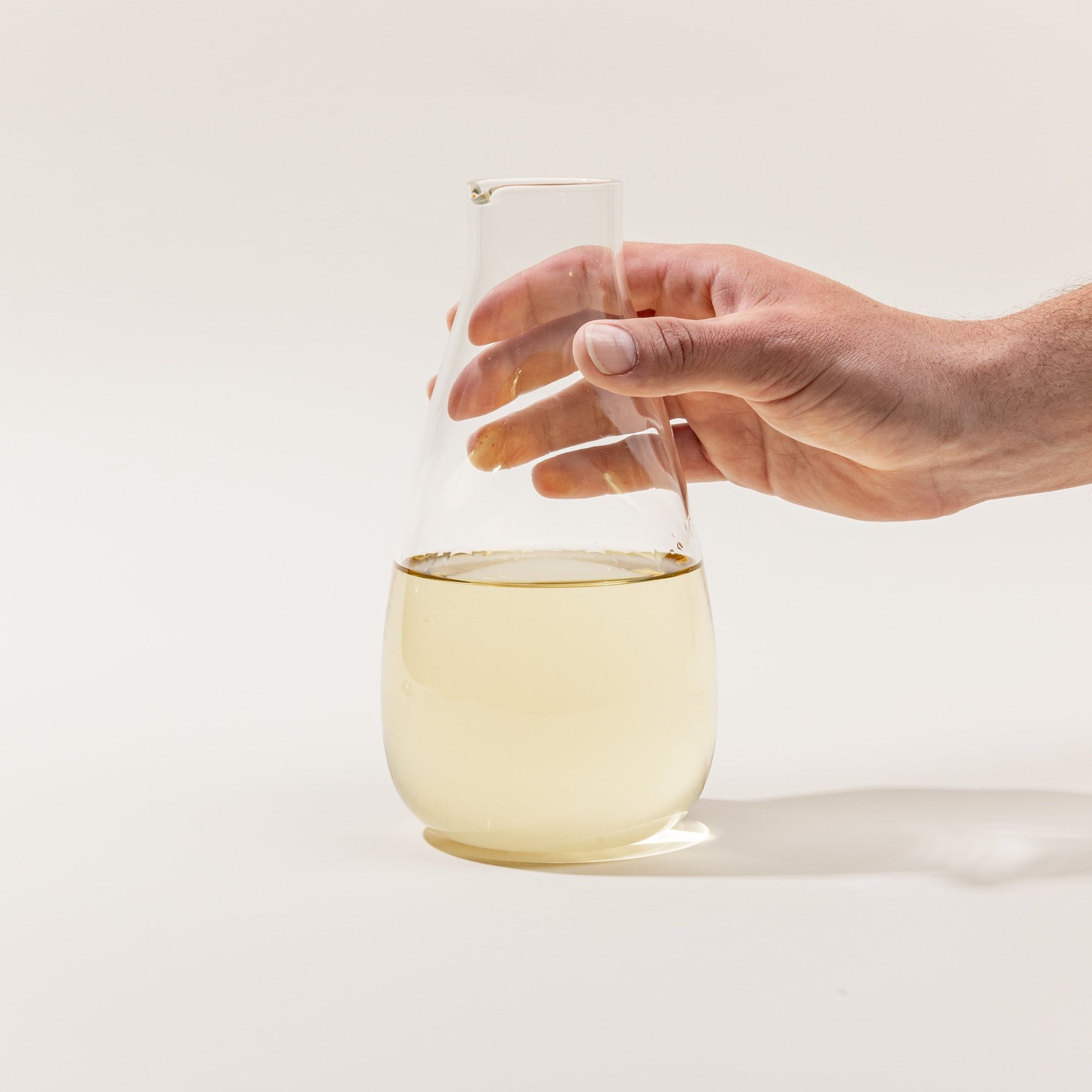 A hand holds a simple elegant clear glass carafe filled with wine.