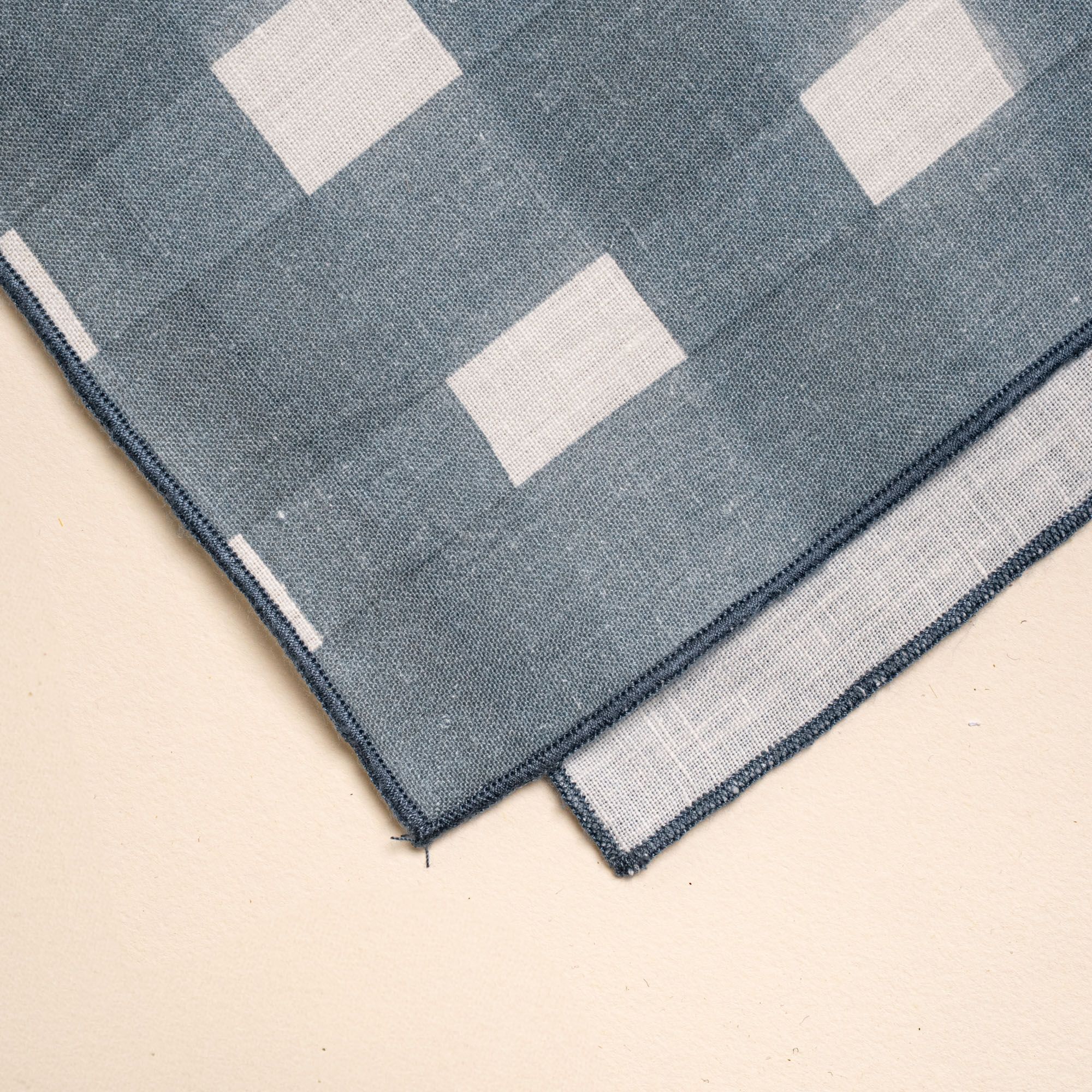 A corner of a table runner folded laying flat featuring a blue-grey crosshatch pattern with navy edges.