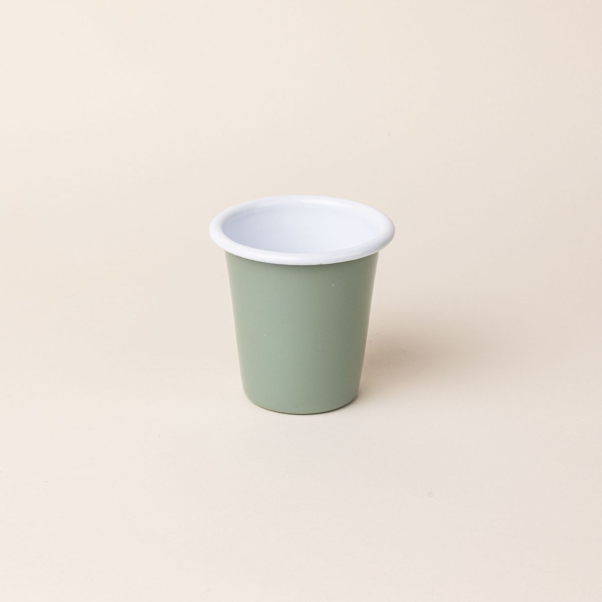 A short enamel cup with a sage green exterior and white interior
