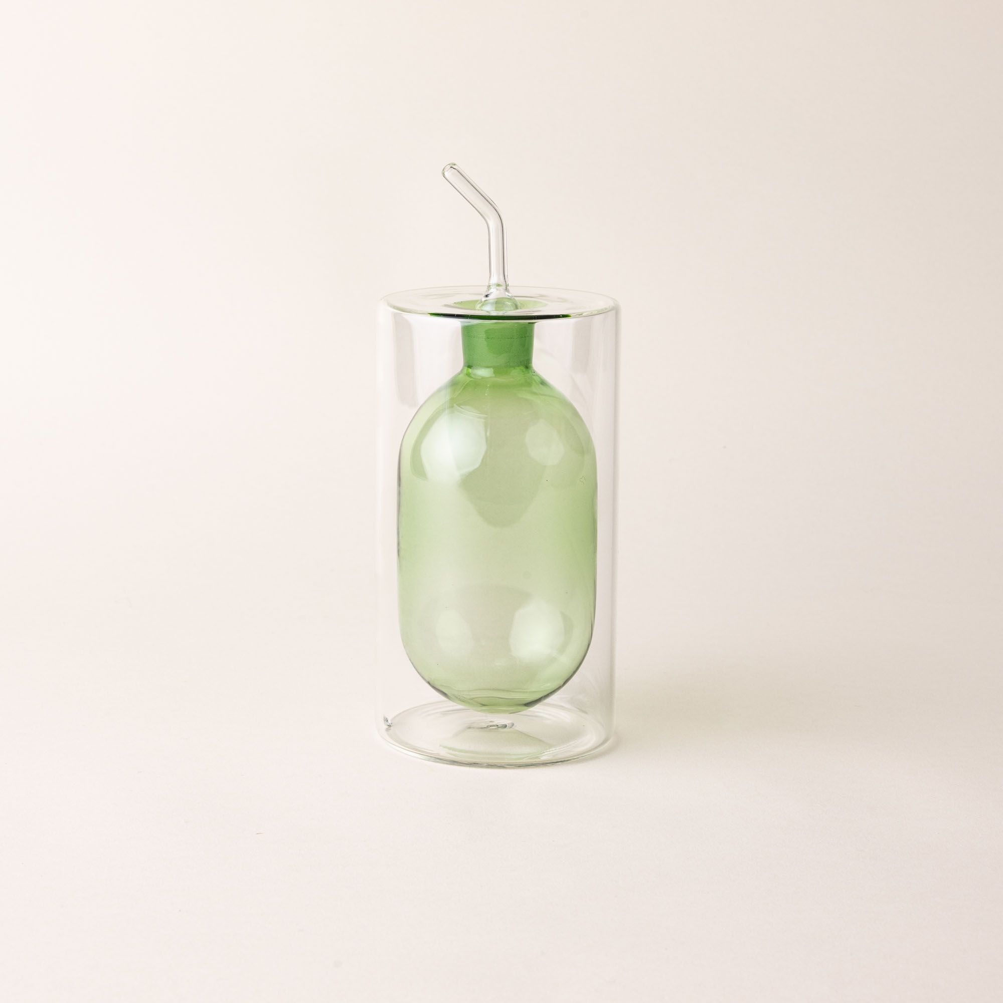 An artful glass cruets in a green color. There is a rounded bulb that acts as a container for the cruet, surrounded by a doubled glass wall.