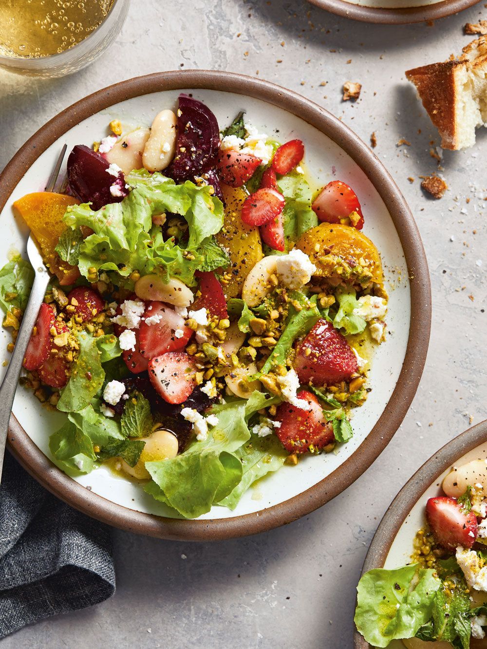 A white dinner plate sits on a table. The plate is filled with a colorful strawberry feta salad.