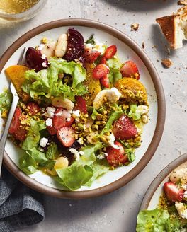 A white dinner plate sits on a table. The plate is filled with a colorful strawberry feta salad.