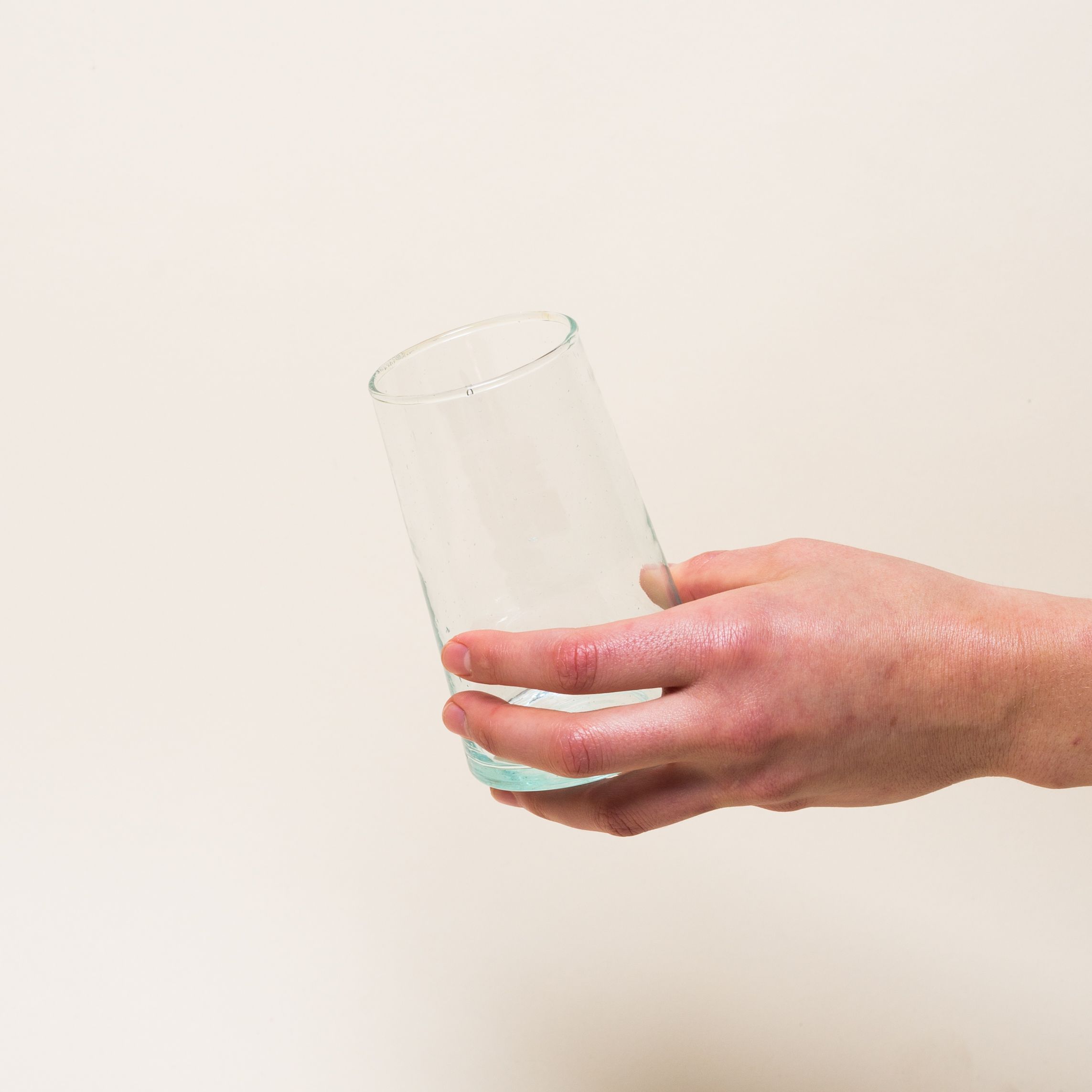 Hand holds a recycled Moroccan glassware tall glass that is empty
