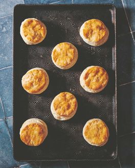 Overhead view of golden biscuits on an oven tray against a blue tile countertop.