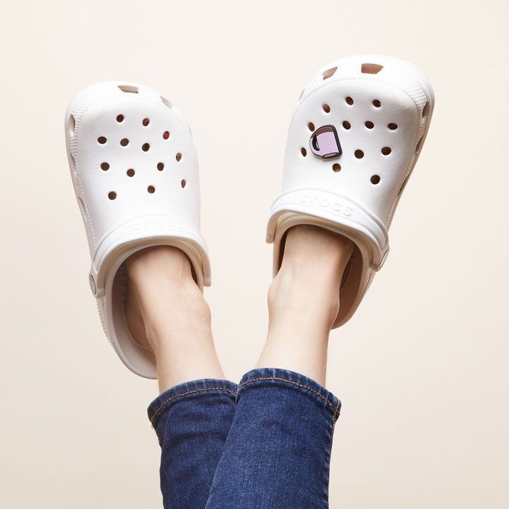 Two feet with Crocs with The Mug charm on it