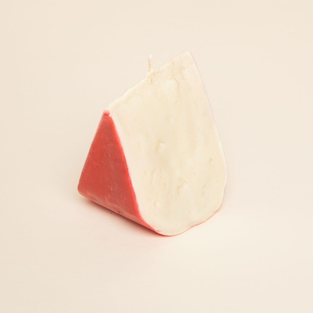 A pale yellow candle stood on its wide edge with a layer of red at the exterior to suggest a wedge of gouda cheese with a red wax rind