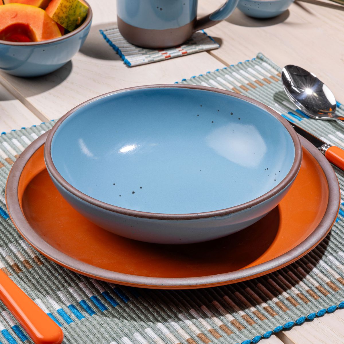 A shallow dinner bowl in a robin's egg blue color sits on a large dinner plate in a bold orange color.