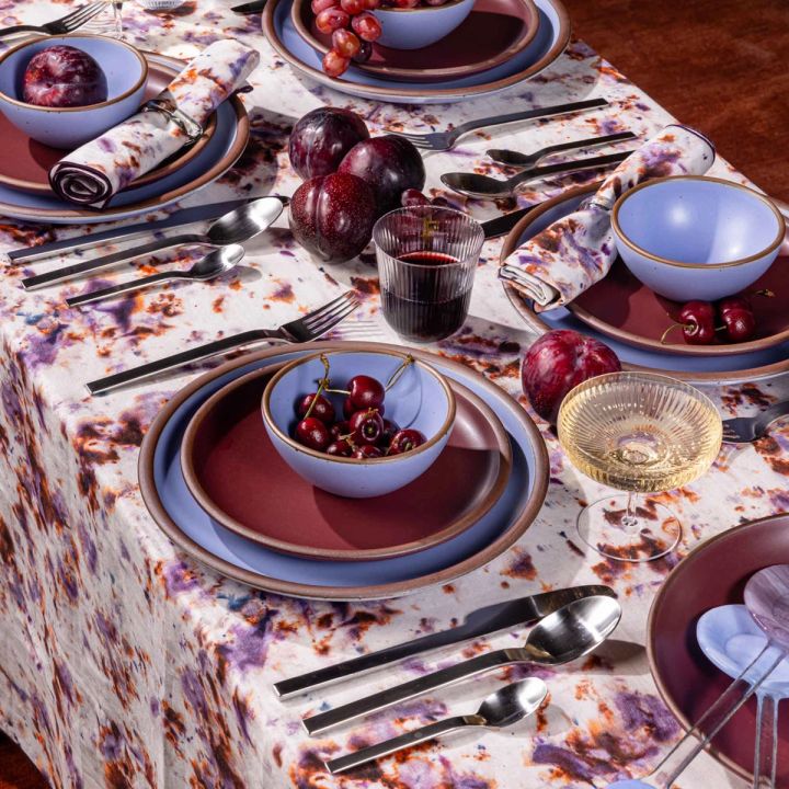 A beautiful tablescape featuring periwinkle and plum ceramic dinnerware, silver flatware, and a marbled purple tablecloth