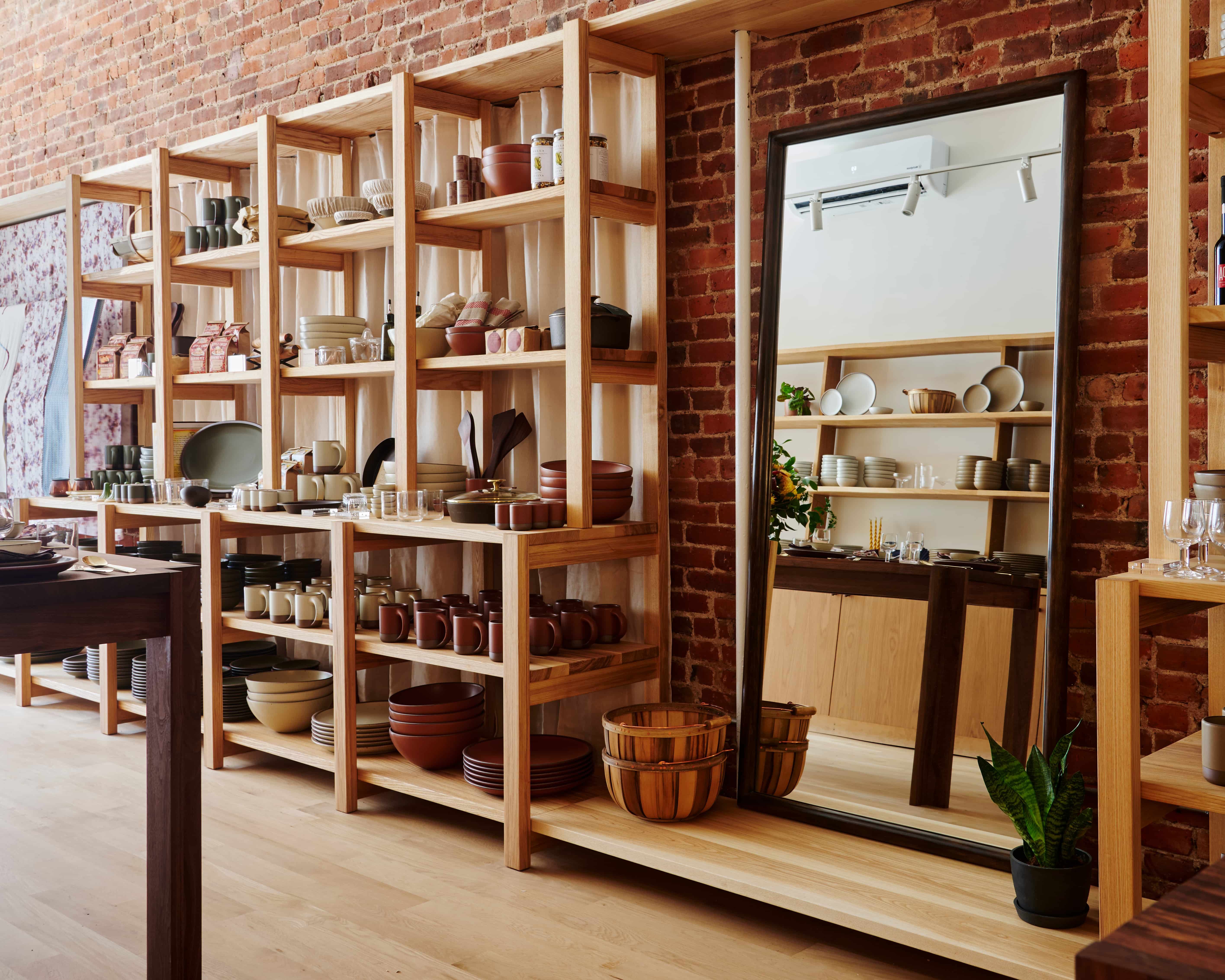 A long built in shelf against a brick wall with a mirror and ceramic bowls and plates fill the shelves