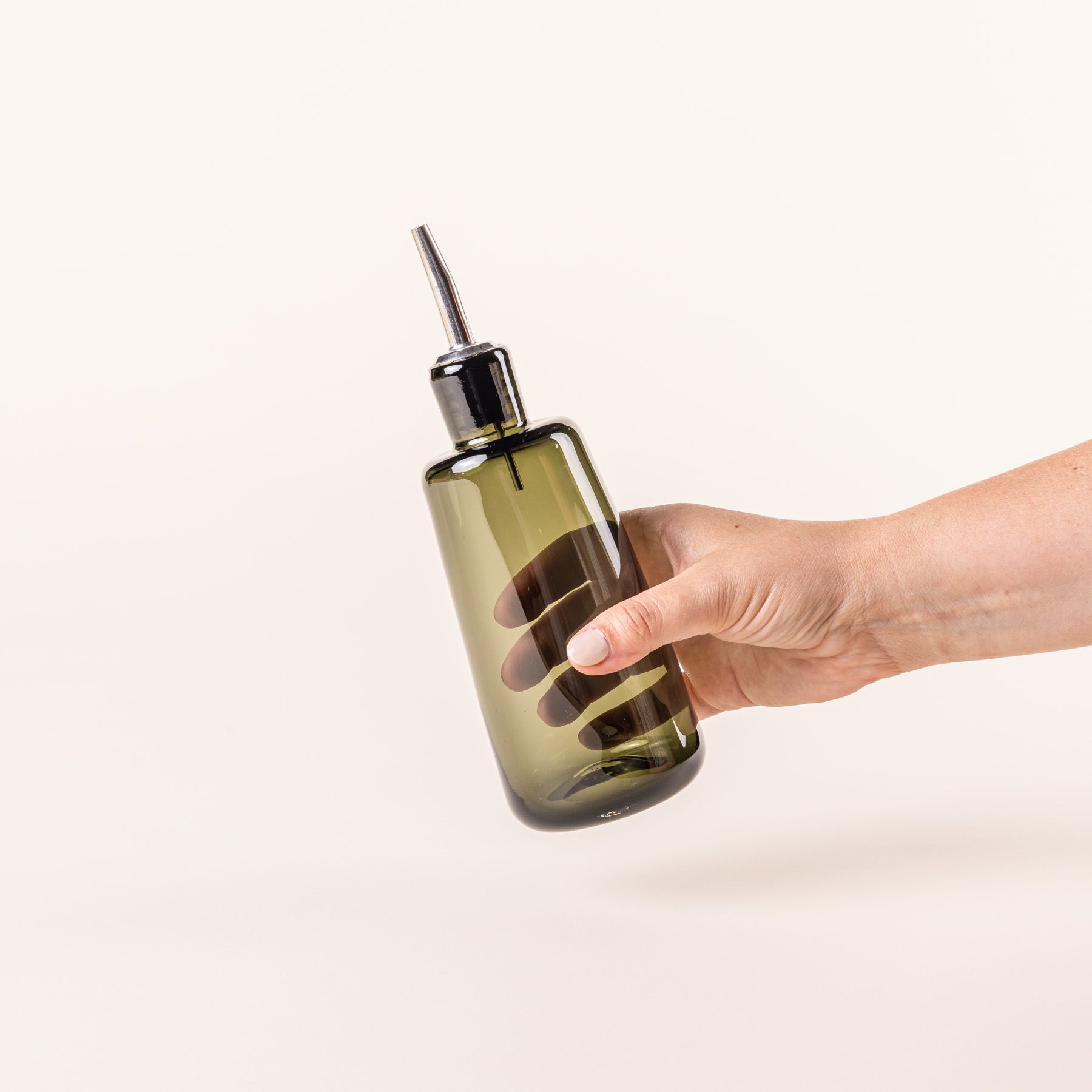 A hand holds a short glass cylindrical cruet in spruce green color