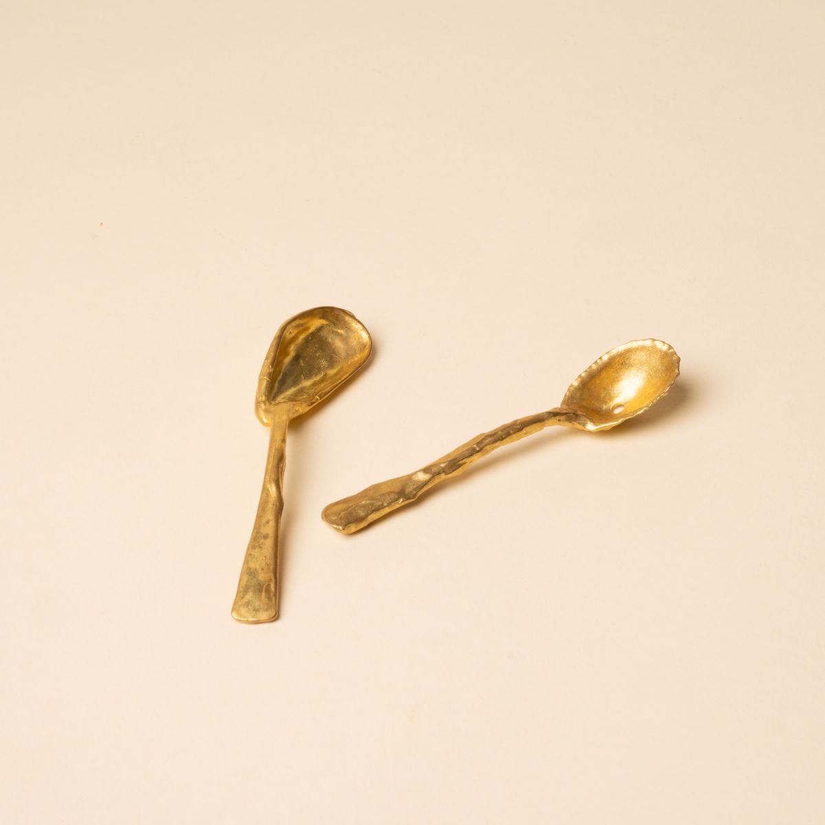 Two small handcrafted gold spoons with textured, organic shapes on a neutral background.