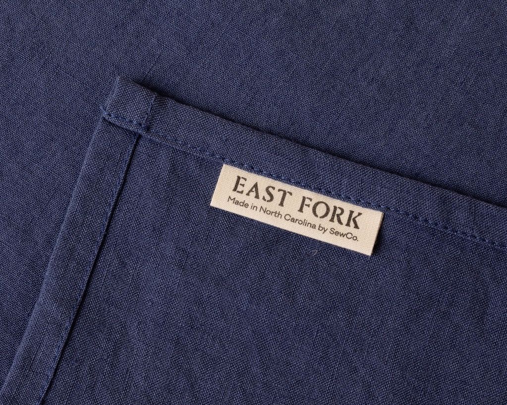 A close up of the corner of a linen napkin with a tag that reads "East Fork - Made in North Carolina by SewCo."
