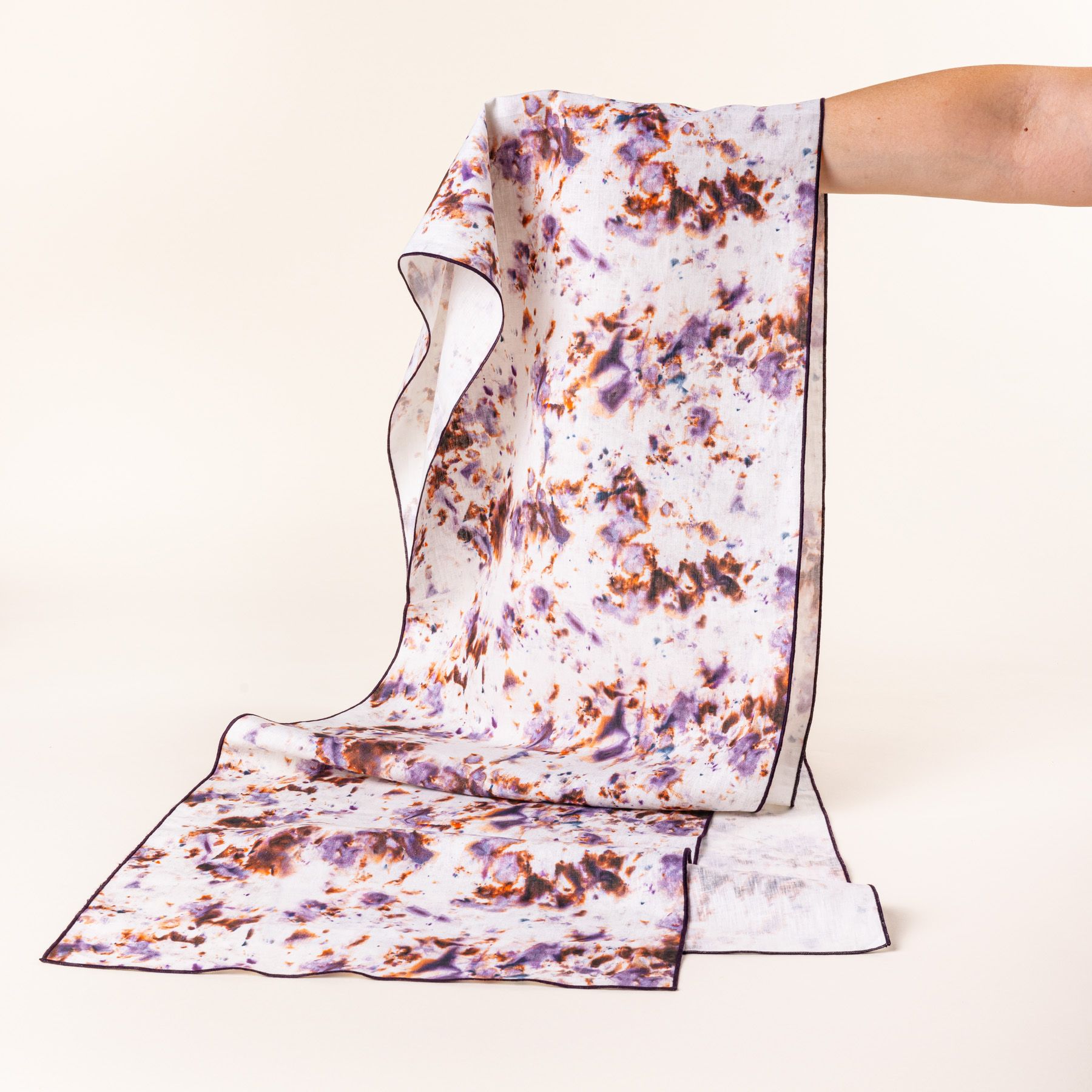 A hand holds up a table runner with a marble pattern featuring pink, purple, orange and white colors folded artfully 