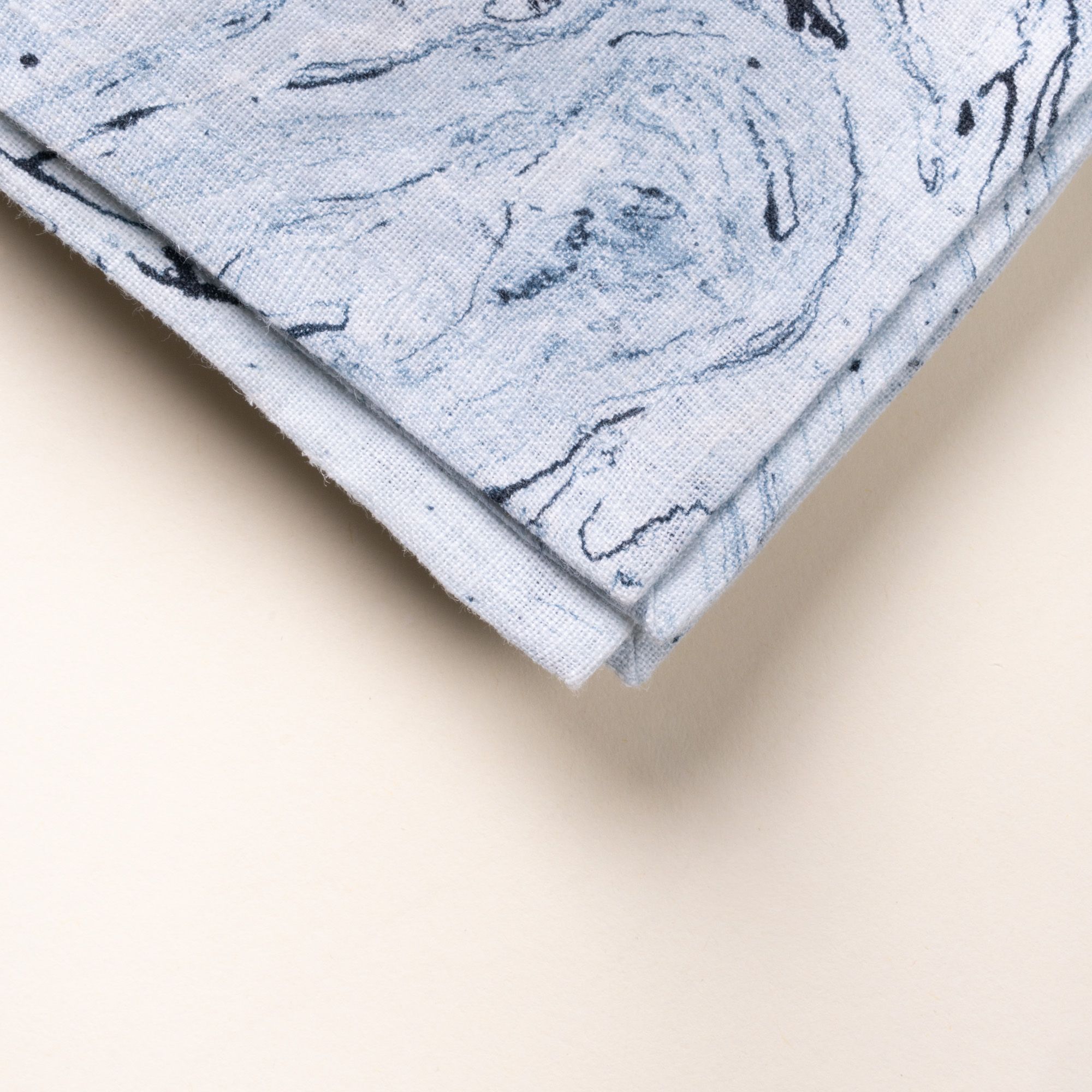 A closeup of the corner of a folded blue marbled cloth napkin with swirling stone-like pattern on a light background.