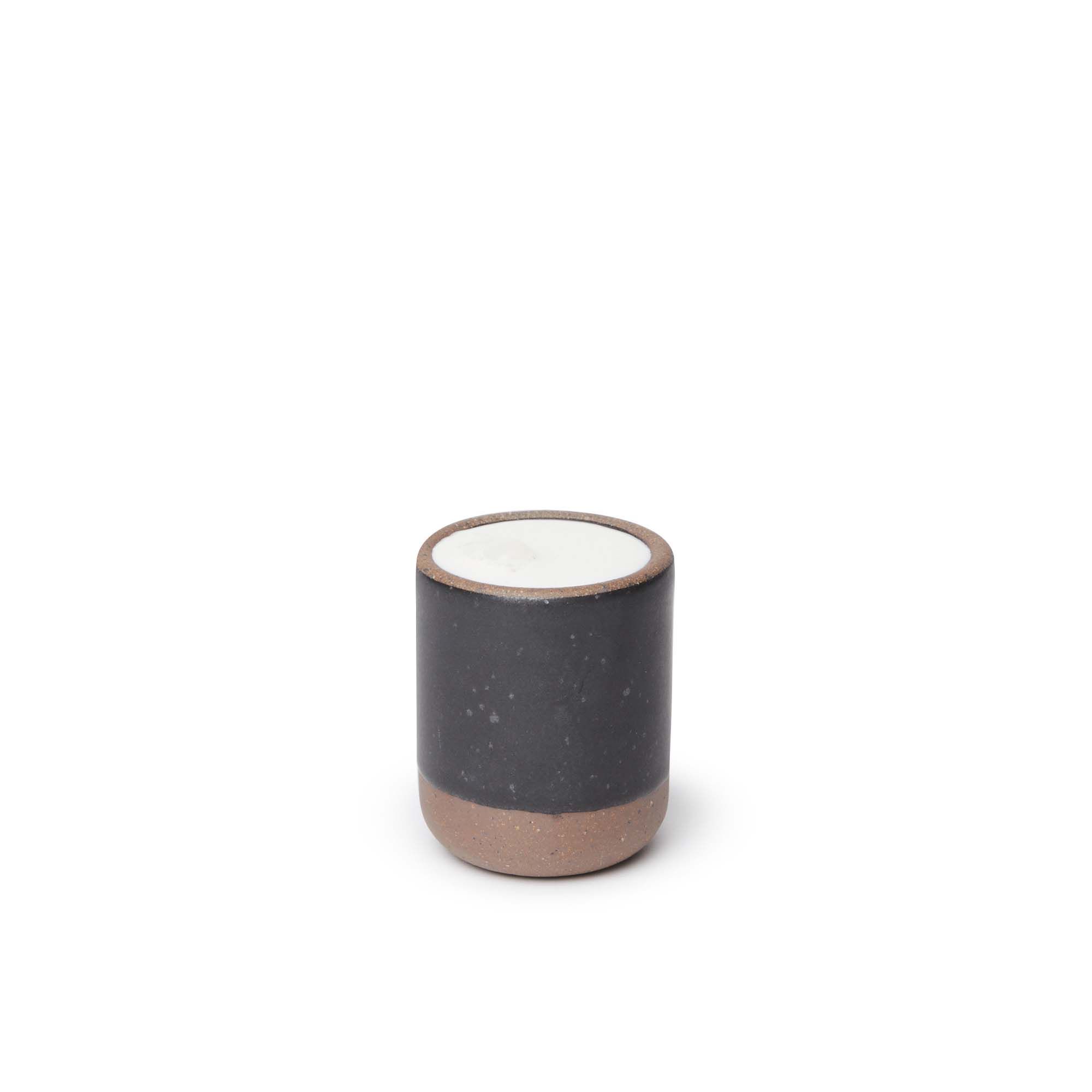 A small, short ceramic mug cup in a graphite black color featuring iron speckles and unglazed rim and bottom base, filled with milk.