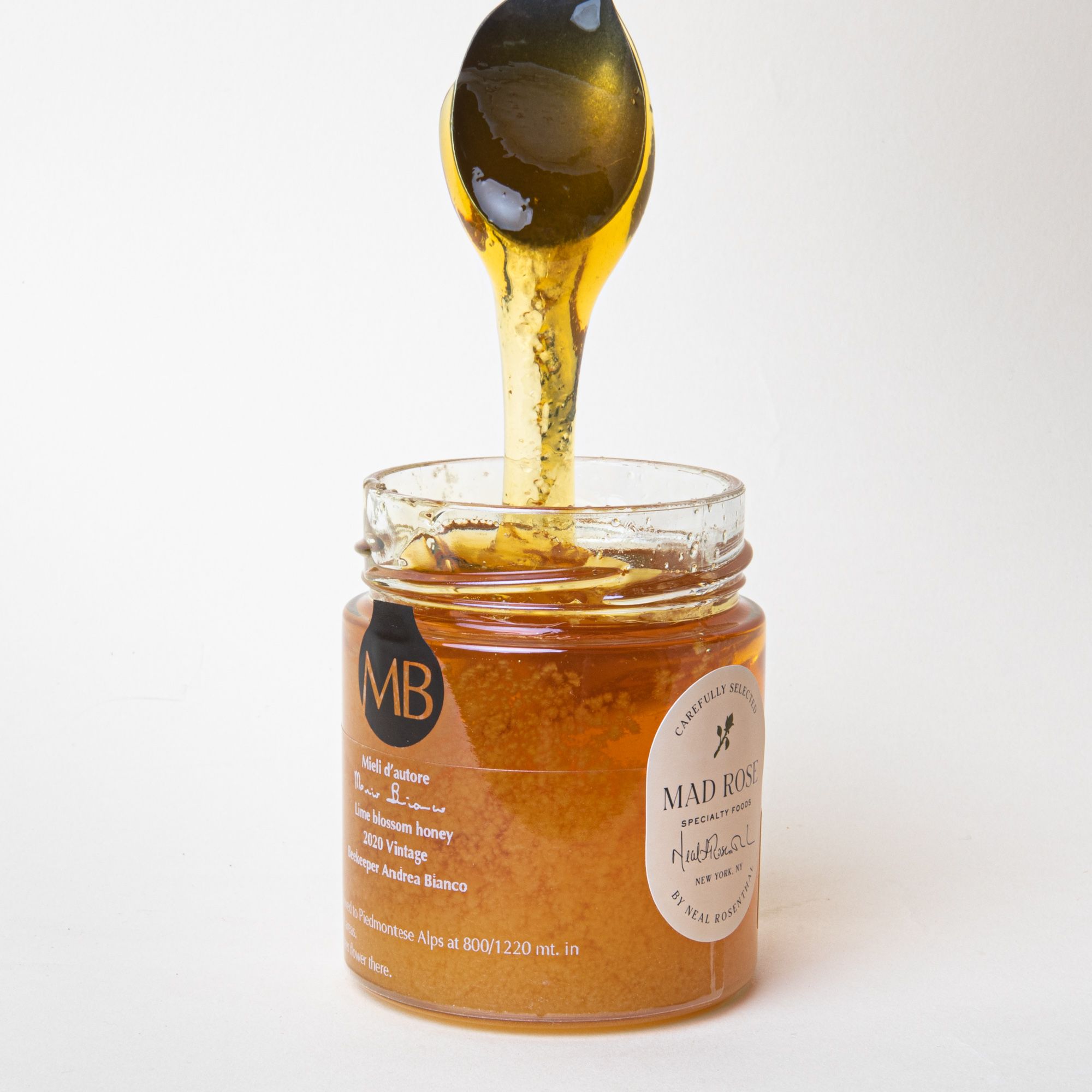 A spoon scooping honey out of a short clear jar with a small white label