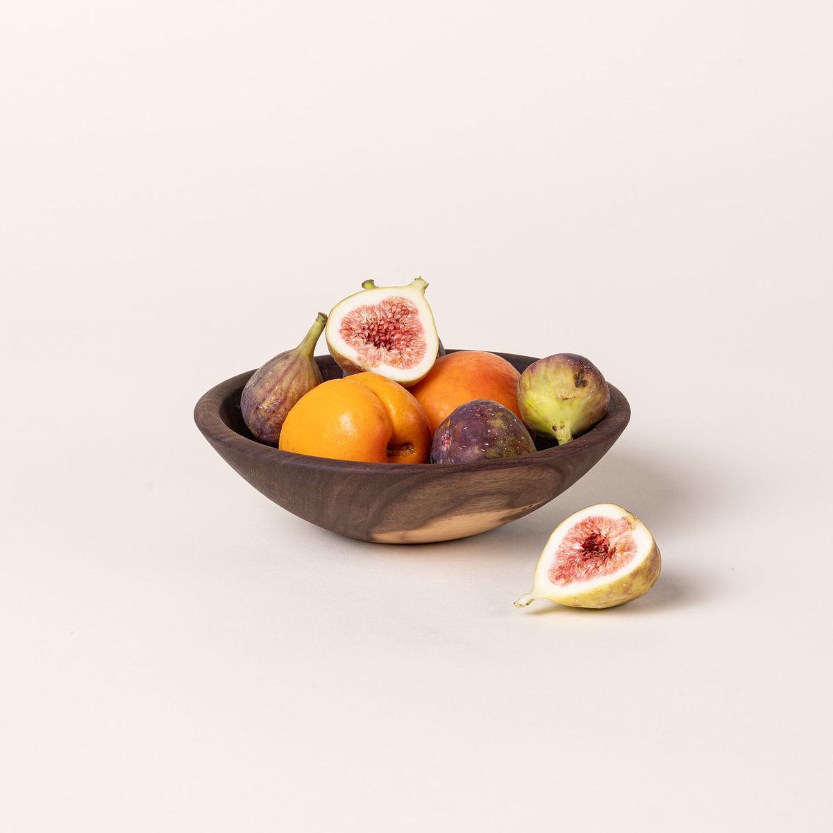 A small walnut wood bowl filled with small fruits like figs and clementines