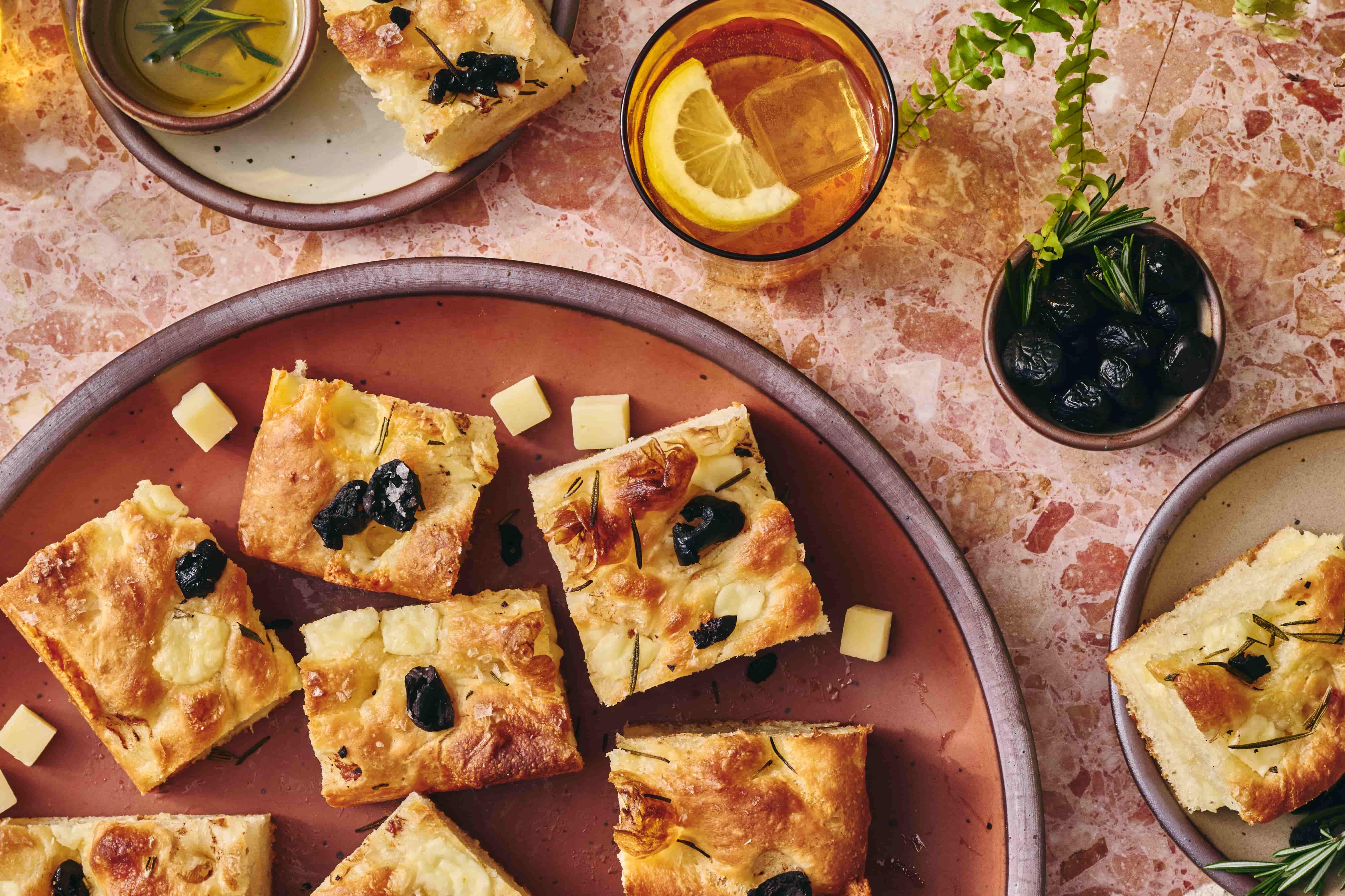Slices of focaccia bread on a large ceramic plate, artfully arranged next to Cabot Creamery cheese cubes, and a glass filled with water and lemon.