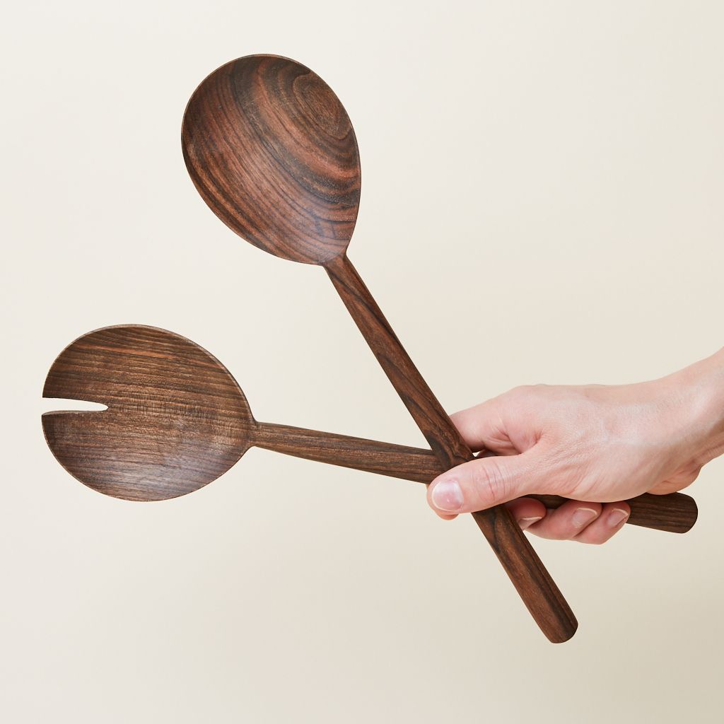 A hand holds a set of two walnut serving spoons, one with a notch removed