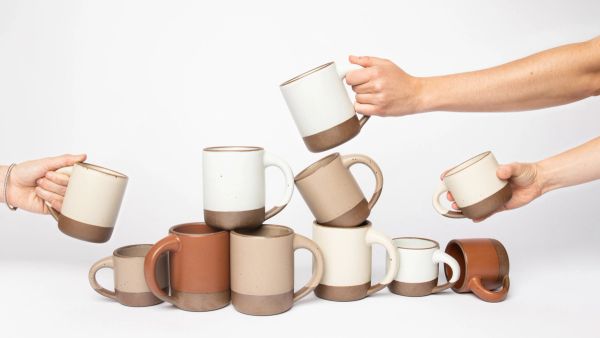 hands holding the small mug, the mug and the big mug around a stuck of different sized mugs