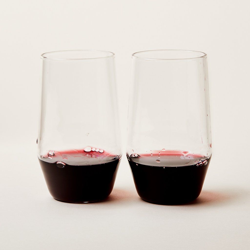 Two tall stemless wine glasses that taper toward the base, filled about one-third with red wine