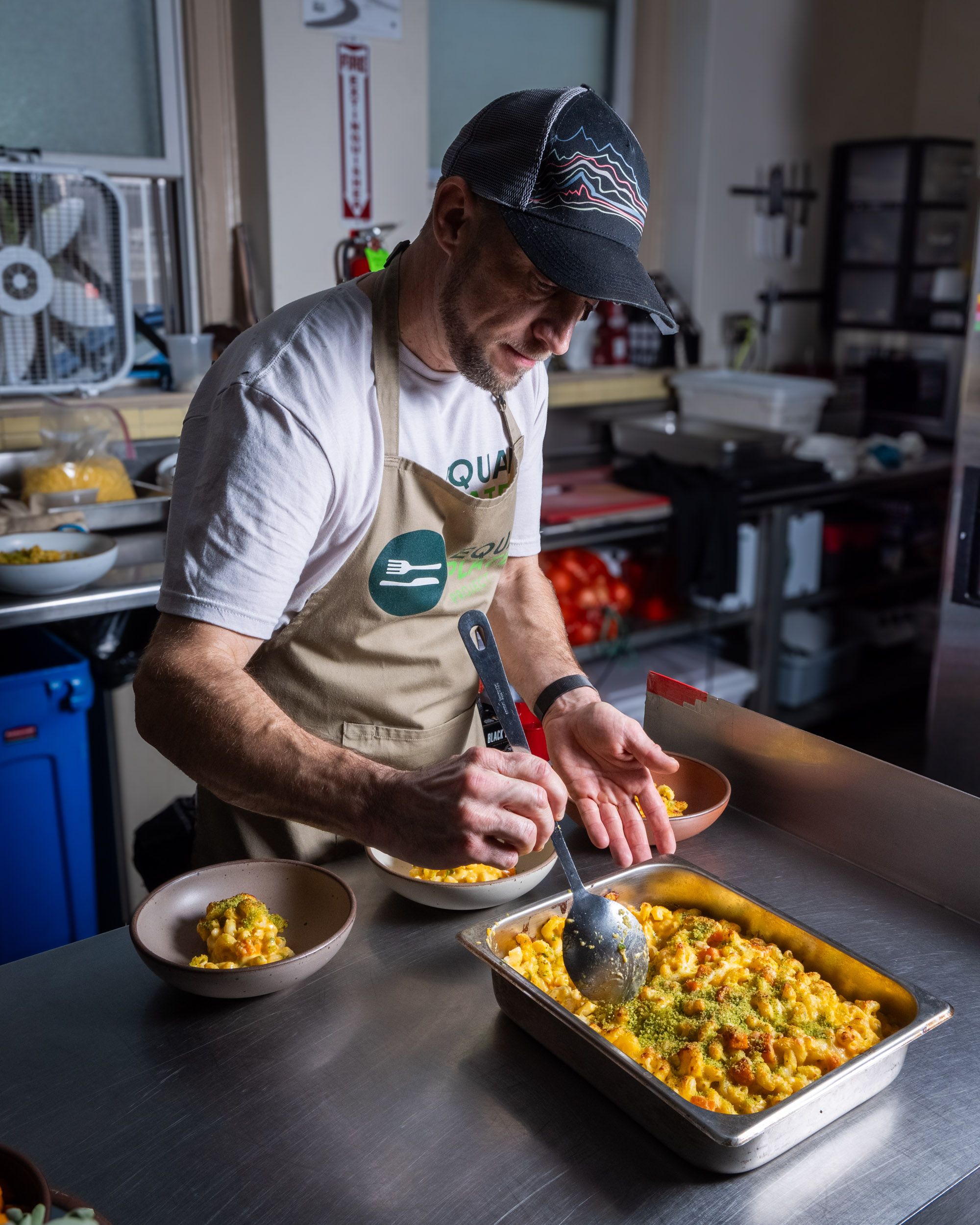 A chef holds a spoon and is scooping some gourmet mac and cheese into bowls from a casserole dish.