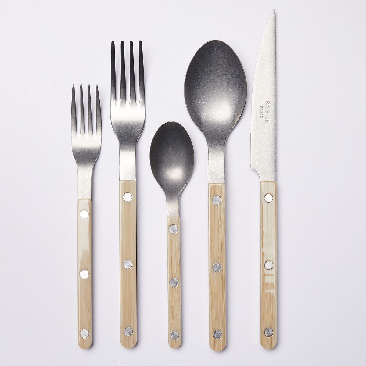 5 piece stylish flatware with matte acrylic handles in light warm tan. In order of salad fork, dinner fork, small spoon, soup spoon, and knife.