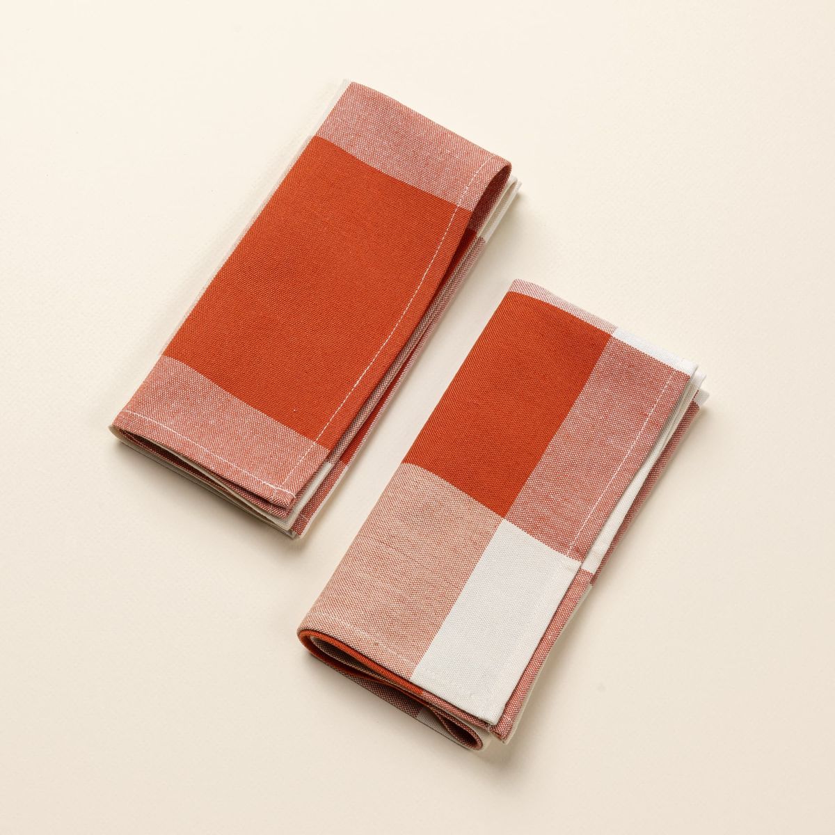 Two folded dinner napkins in a rust and cream gingham pattern.