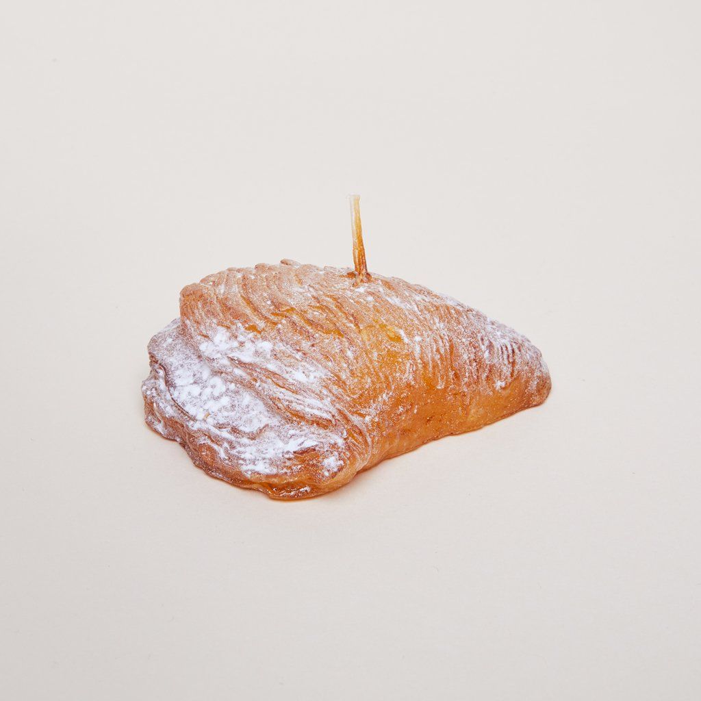 A candle with wick standing up from top center that has the size, shape and texture of a puff pastry
