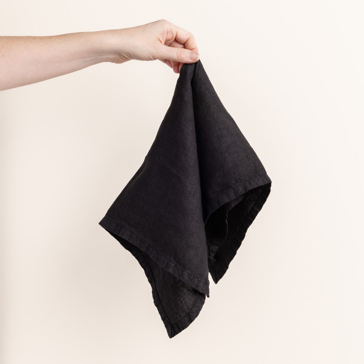 Hand holding a linen napkin in a graphite color from the center 