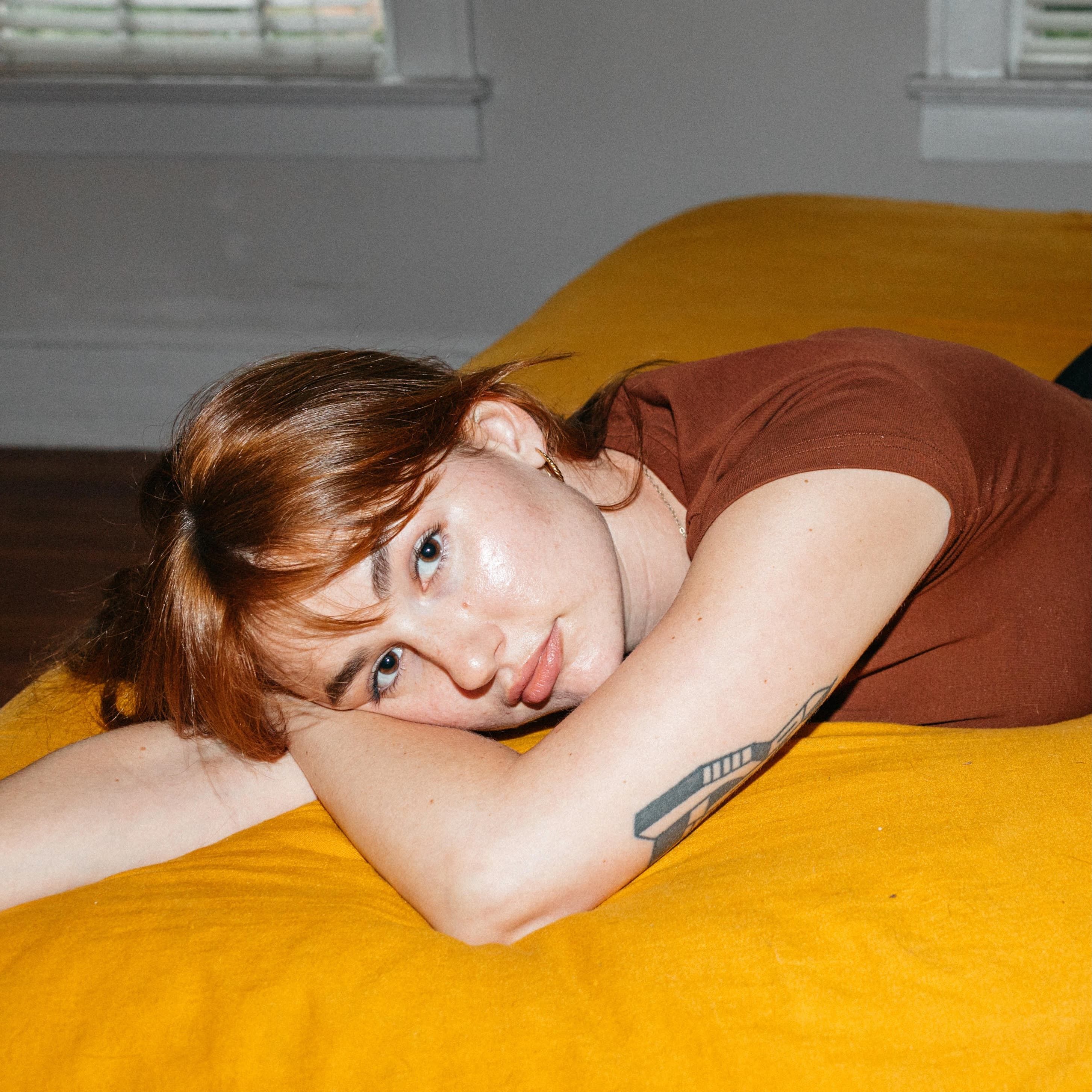 A person is laying down and looking up at the camera slightly smiling.