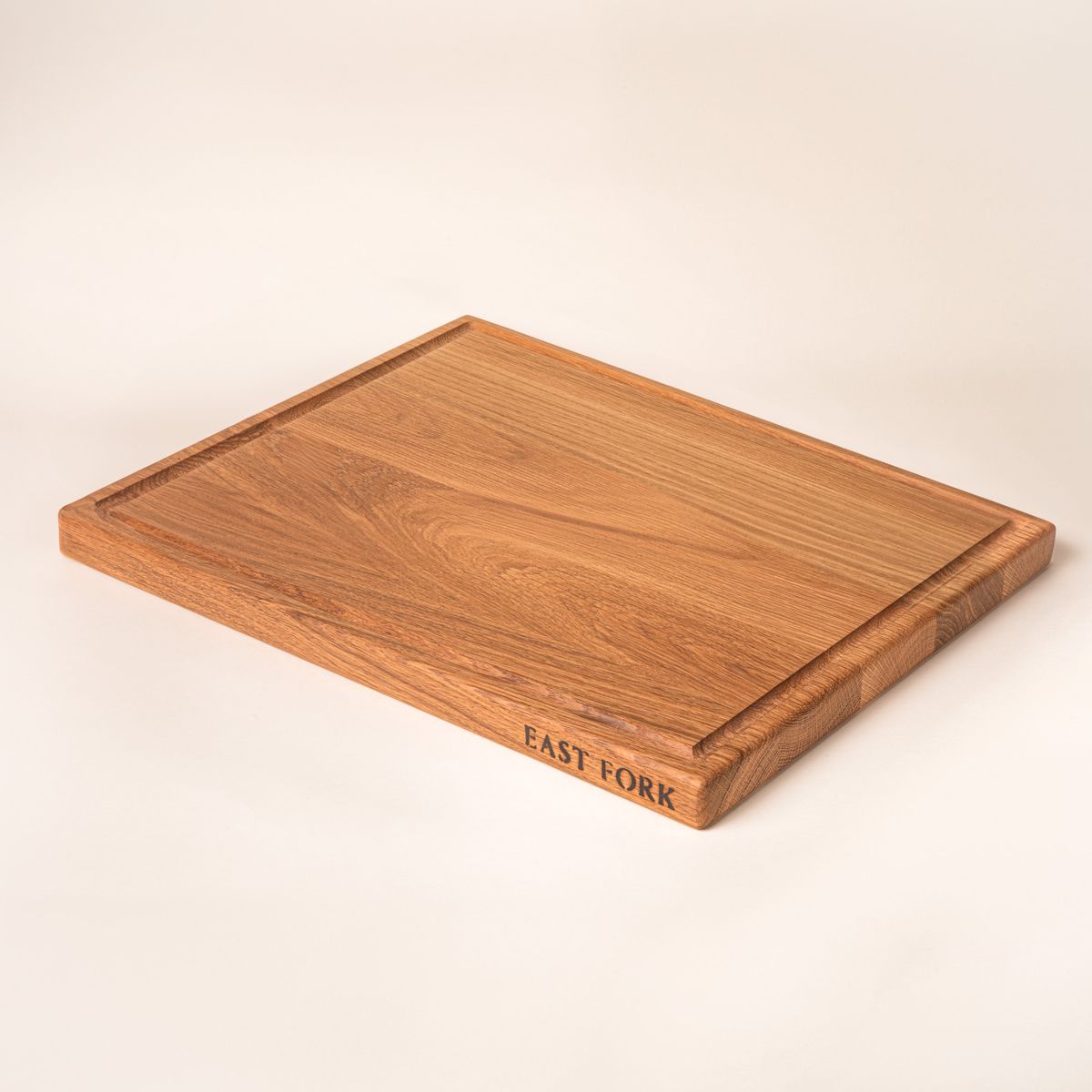 A large rectangular white oak cutting board on its side with a juice groove and an engraving on the edge that reads 'East Fork'