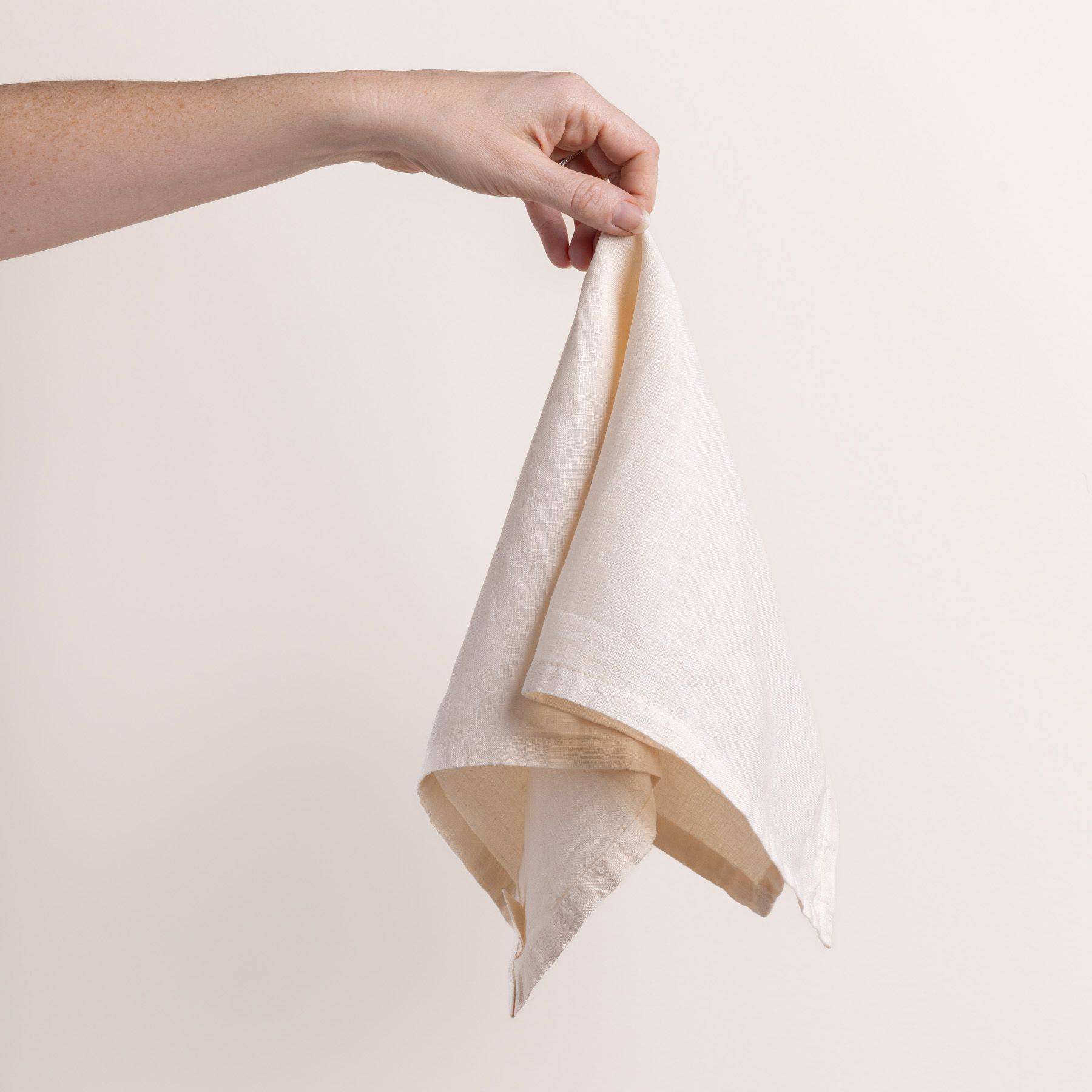 Hand holding a linen napkin in an off-white color from the center 