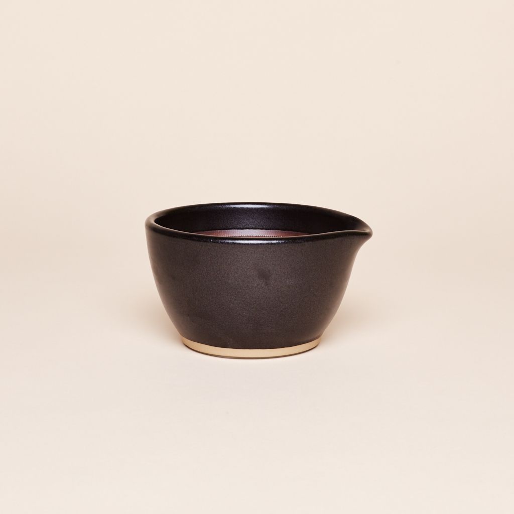 Black mortar with tan base with a round top edge, flared on one side to create a spout.