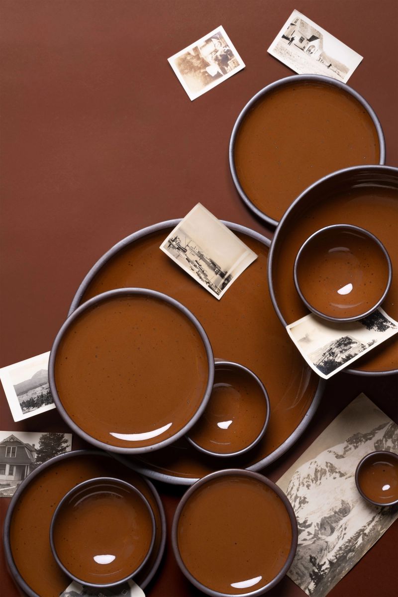 Arrangement of glossy caramel brown ceramic plates and bowls with scattered vintage black-and-white photographs.