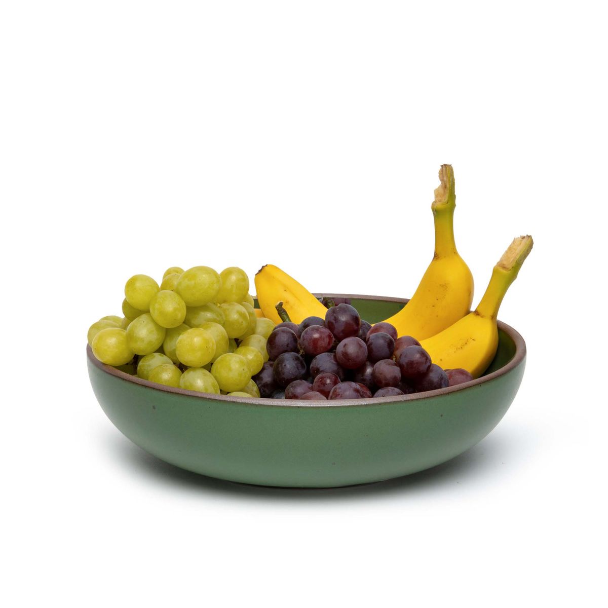 Fruit in a large shallow serving ceramic bowl in a deep, verdant green color featuring iron speckles and an unglazed rim.