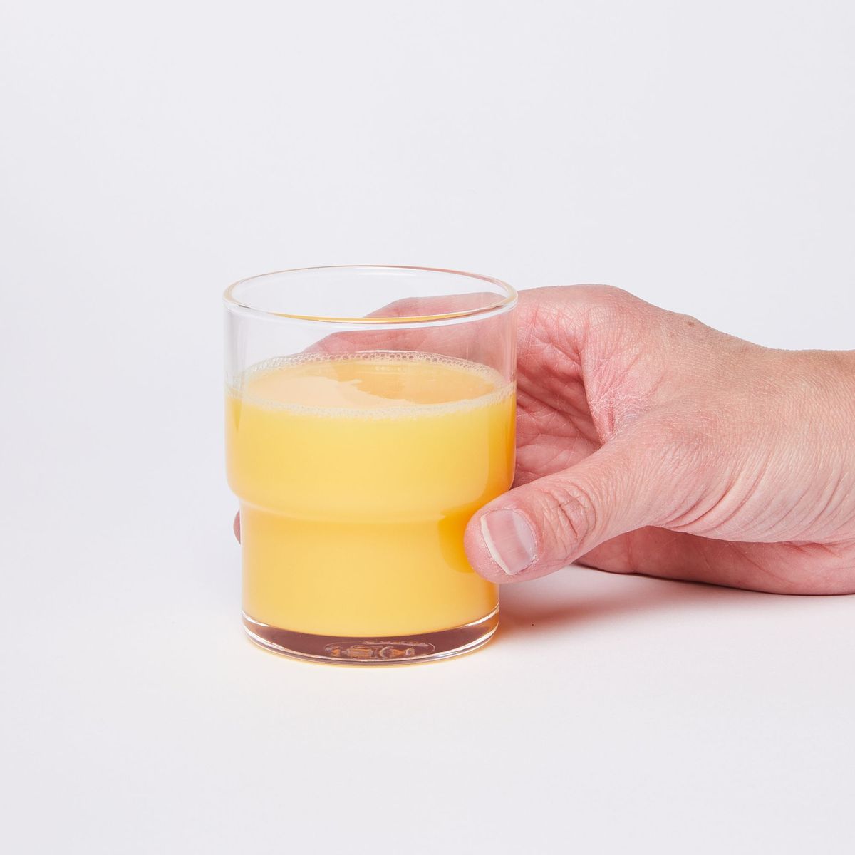 Hand holding a clear cylindrical glass with a wider top half with a narrower bottom half, full of orange juice