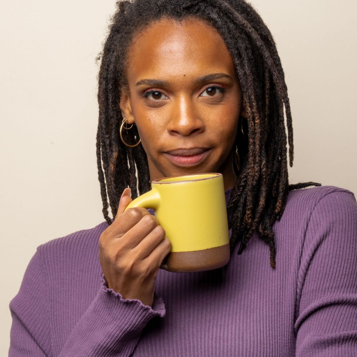 A woman stares at the camera and is holding the mug in a zesty yellow color close to her face.