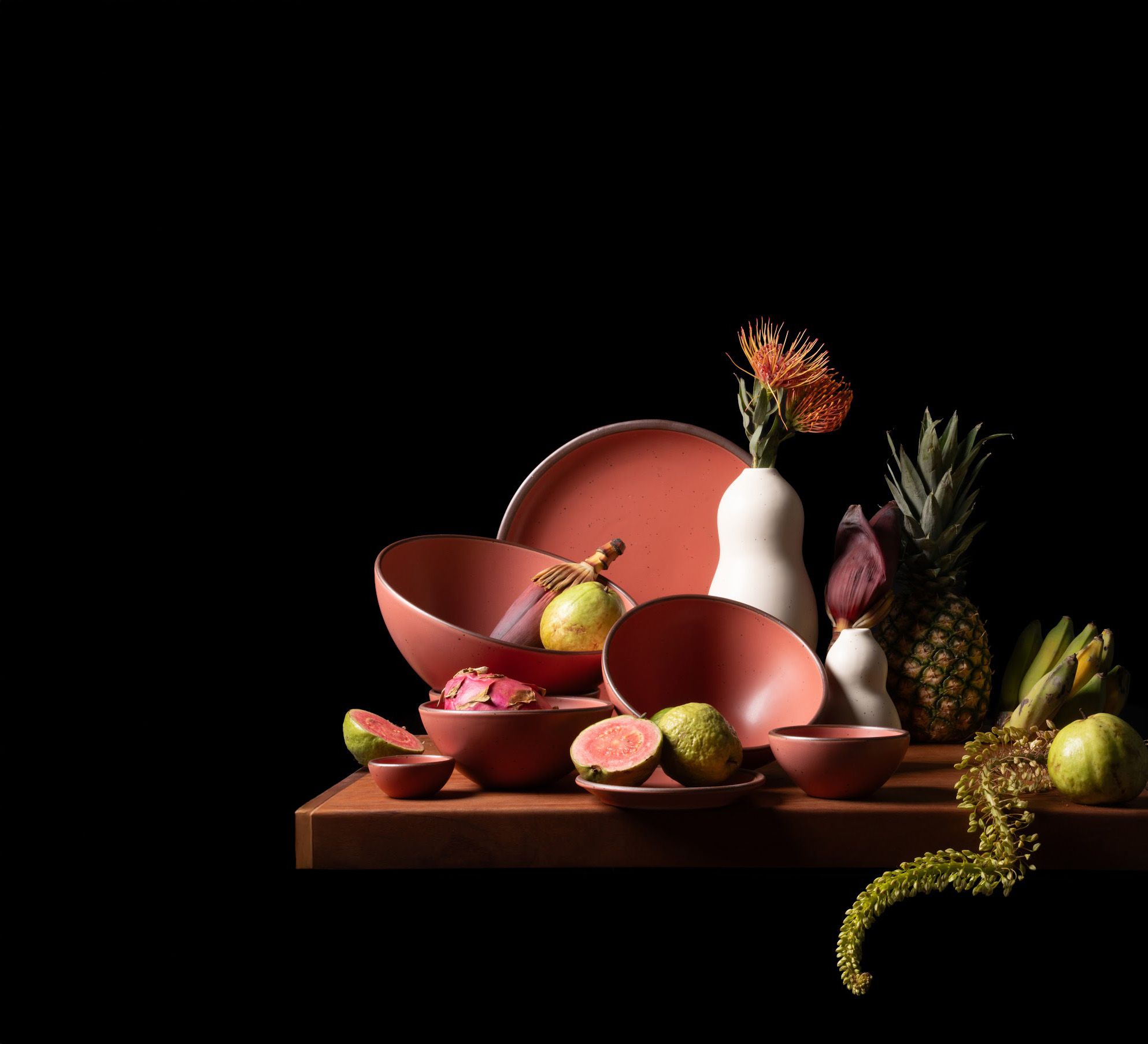 Watermelon pink ceramics with tropical fruit and florals—vivid color and rich texture in a bold tabletop scene.