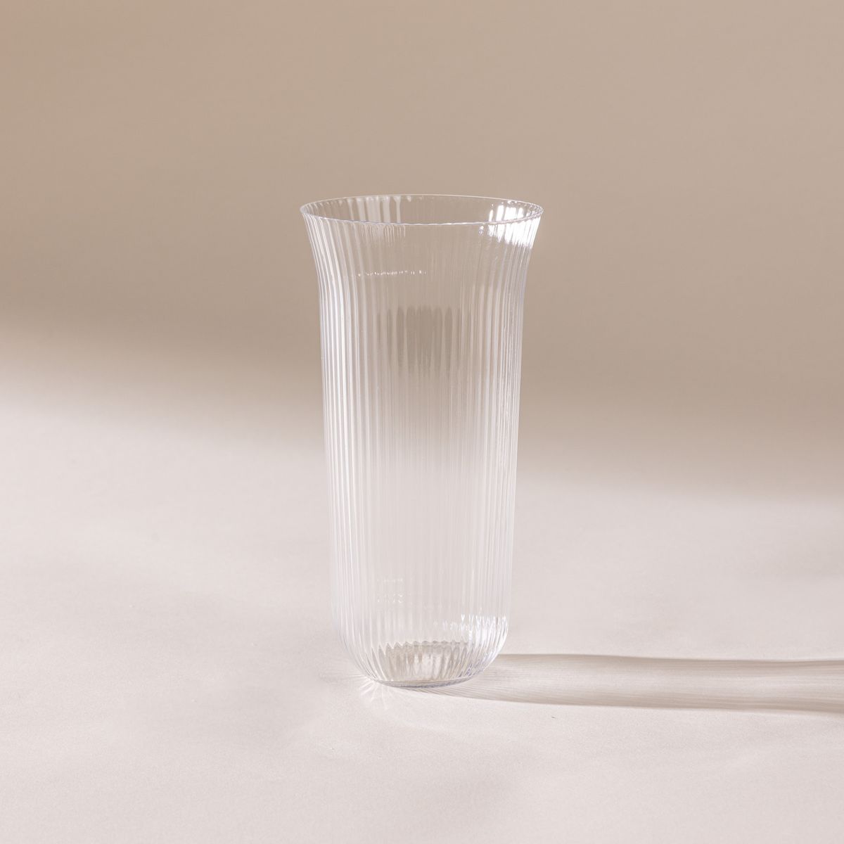 A delicate ribbed tall glass that has a rounded curve on the bottom and curves out on the top.