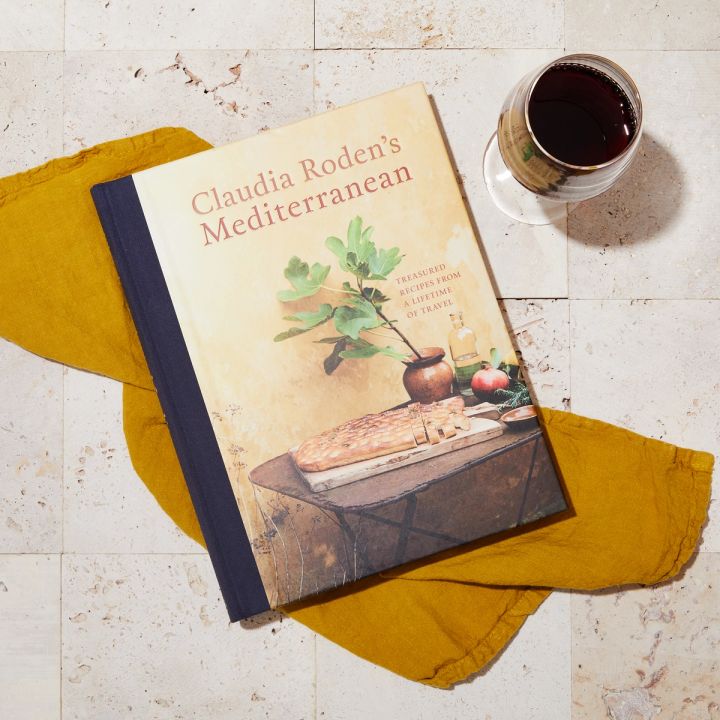 Book laying over an ochre napkins on a tiled surface next to a glass of red wine