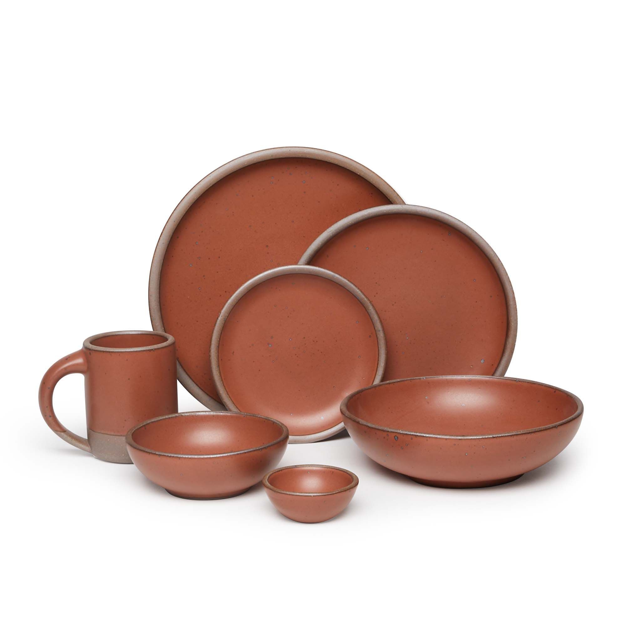 The Mug, bitty bowl, breakfast bowl, everyday bowl, cake plate, side plate and dinner plate paired together in a cool burnt terracotta color featuring iron speckles