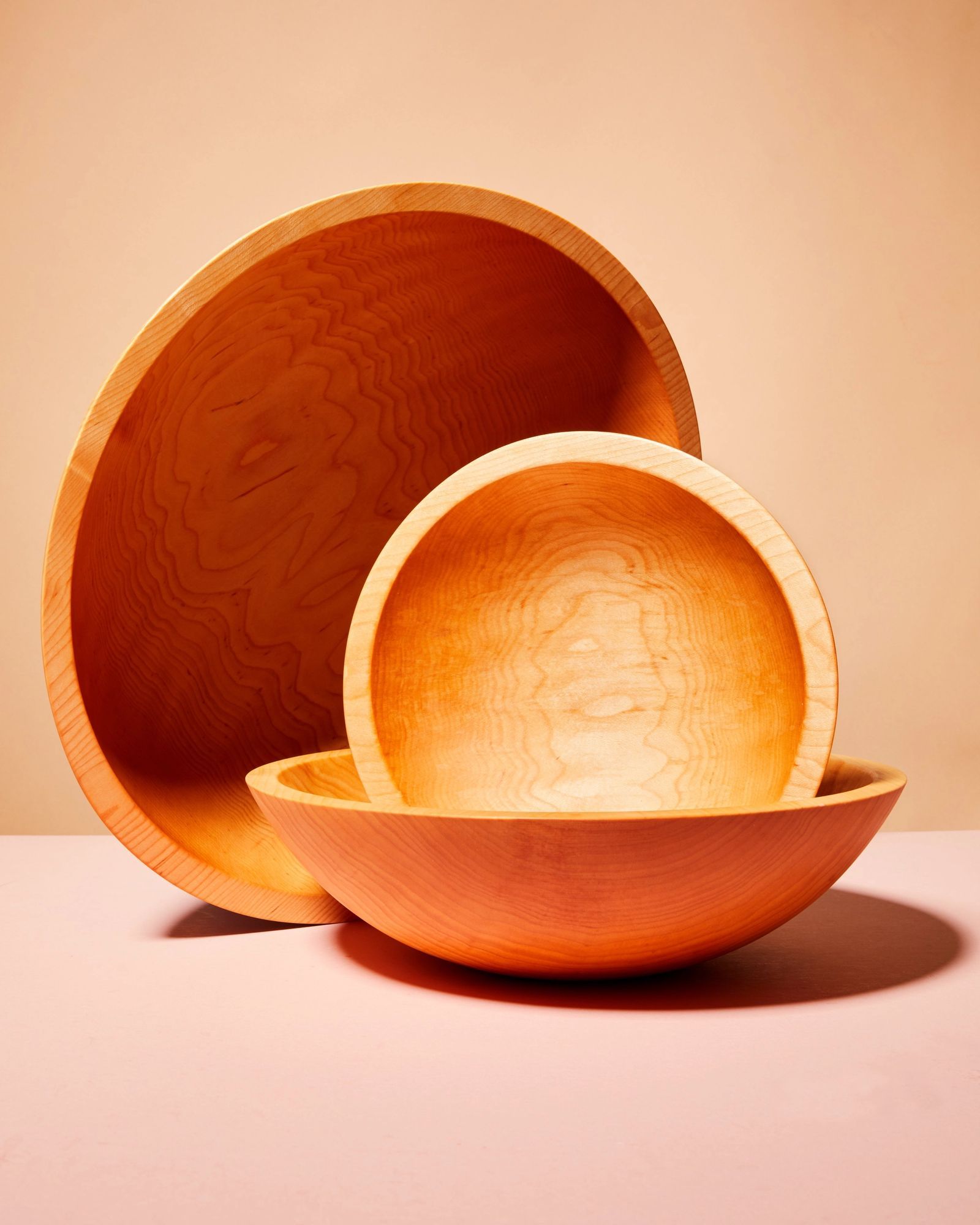 Three various sizes of light tan maplewood salad bowls each artfully arranged together